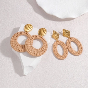 Bohemian woven straw and gold geometric drop earrings on minimalist stone display