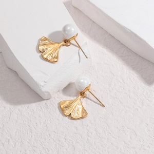 Golden ginkgo leaf stud earrings with white pearls on a minimalist white stone background