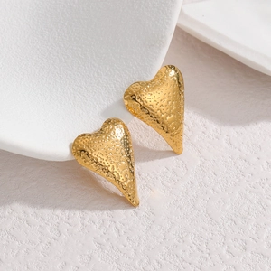 Fashionable golden hammered heart stud earrings made of textured stainless steel on white prop