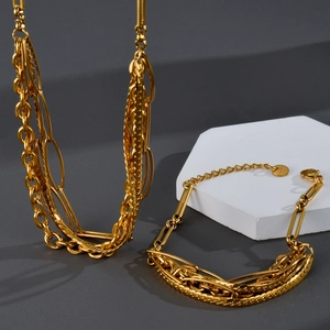 Layered gold stainless steel jewelry set featuring snake and link chains on white podium