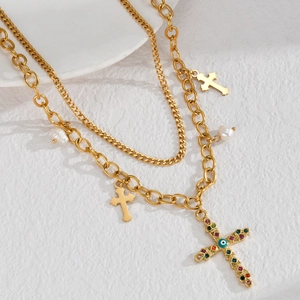 Dettaglio collana dorata a strati con croci, occhio del diavolo e perle su pietra bianca