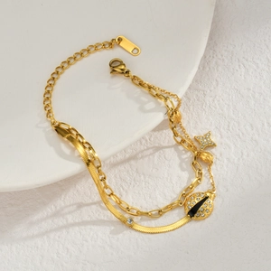 Detail of layered gold bracelet featuring ladybug and pavé star charms on snake chain