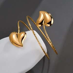 Detailed view of gold spiral cuff bracelet with dual heart-shaped charms and textured band