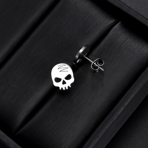 Detailed close-up of silver skull earrings with butterfly backing on black texture