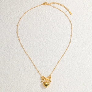 Chic gold bow and heart pendant necklace with satellite chain on a textured surface