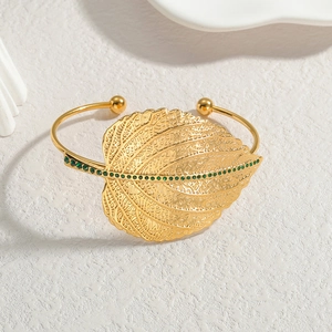 Gold leaf open bracelet with green stones on white textured background in minimalist style
