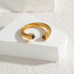 Golden twisted cable cuff bracelet with dark spherical gemstone beads on a white stone base