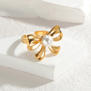 Elegante anello con fiocco dorato e perla centrale su base di pietra bianca moderna