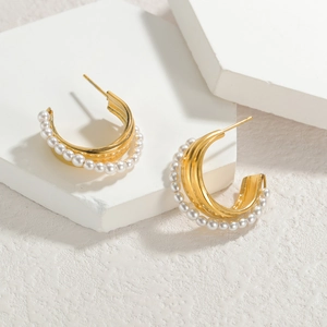 Elegant gold C-shaped hoop earrings with white pearls on a minimalist stone background