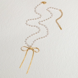 Elegante Perlenkette mit goldenem Schleifenanhänger und S-STEEL-Anhänger auf Texturhintergrund