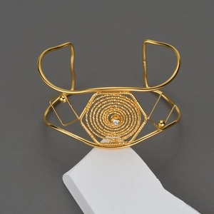 Dettaglio del bracciale dorato con trama a spirale esagonale e cristallo centrale lucido