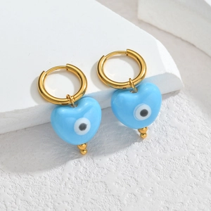 Gros plan de boucles d'oreilles créoles dorées avec pendentif œil bleu en forme de cœur