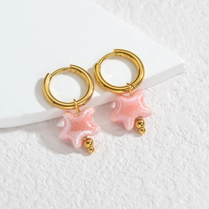 Détail de boucles d'oreilles créoles dorées avec pendentifs étoiles en céramique rose