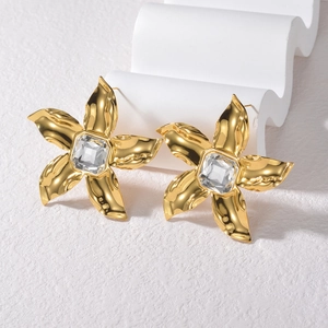 Elegant gold flower earrings with zircon center displayed on a white wave stand
