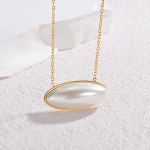 Minimalist double layer gold necklace with a large oval white faux pearl pendant on marble