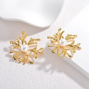 Gold snowflake earrings with center pearl on a minimalist white textured background