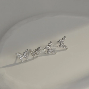 Detail of four silver butterfly earrings with sparkling cubic zirconia on a white plate