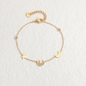 Gold stainless steel bracelet featuring star and moon charms on a textured stone surface