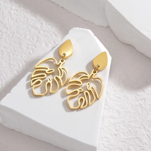 Détail de boucles d'oreilles feuilles de monstera dorées sur bloc de pierre blanc