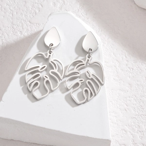 Gros plan de boucles d'oreilles monstera en acier inoxydable sur un socle en pierre