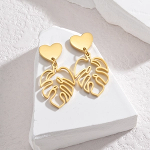 Gros plan de boucles d'oreilles feuille de monstera dorées avec clous en forme de cœur