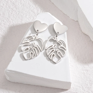 Détail de boucles d'oreilles feuilles évidées argentées sur pierre blanche texturée