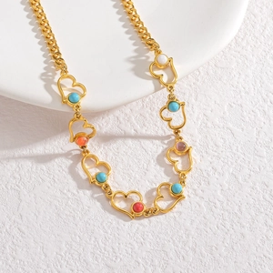 Détail du collier cœur doré orné de perles multicolores sur une surface blanche
