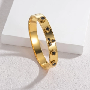 Elegante bracciale rigido dorato con ciondoli a stella neri e bordi con perline