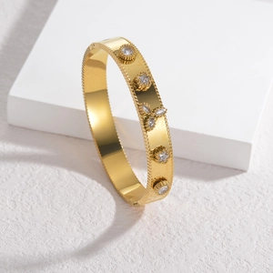 Elegante bracciale rigido dorato con cristalli a stella e bordo perlato su sfondo bianco