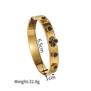 Gold stainless steel bangle featuring four-leaf clover black gem inlays on white background