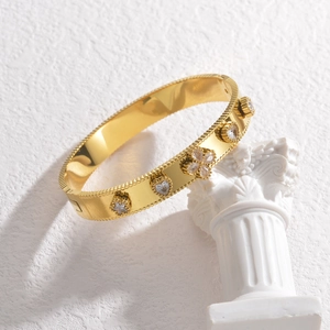 Gold stainless steel bangle with clover heart charms and zircons on a white pedestal