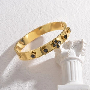 Gold stainless steel bangle with black clover and heart charms on white column