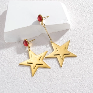 Asymmetric gold star drop earrings with deep red resin accents on white display