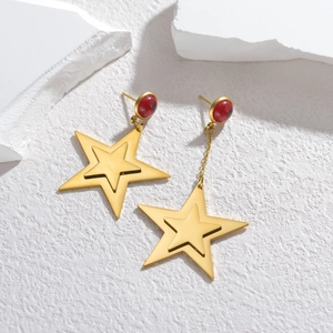 Asymmetric gold star drop earrings with ruby-red beads on a textured stone surface