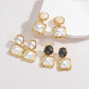 Close-up of geometric pearl earrings in cream, white and black marble textures on stone