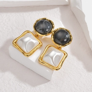 Elegant geometric gold earrings with marble and mother-of-pearl inlays on a stone surface