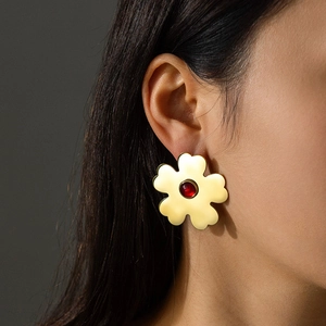 Gold five-petal flower earrings with red gemstone center worn by model on dark background