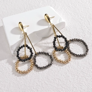 Chic gold teardrop earrings with beaded tassel rings on a minimalist white stone pedestal