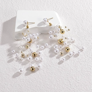 Longues boucles d'oreilles perles et perles dorées sur support blanc minimaliste