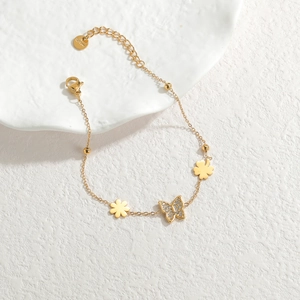 Bracelet en acier inoxydable doré avec pendentifs papillon et fleur sur plateau blanc