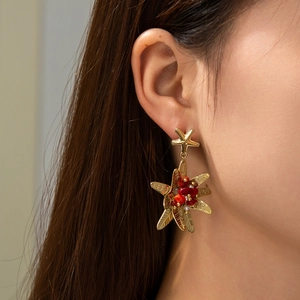 Boucles d'oreilles étoile de mer dorées avec pierres rouges portées par un mannequin