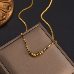 Collier minimaliste à chaîne box avec perles dorées présenté sur un coffret à bijoux