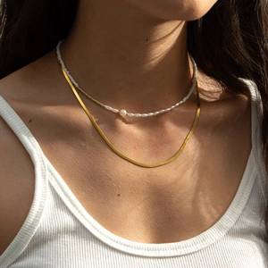 Double-layered gold snake chain and white pearl necklace worn on a female model