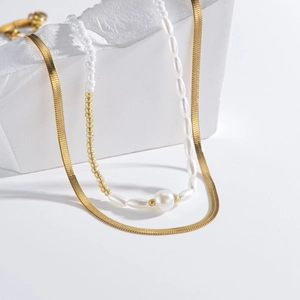 Double-layered gold flat snake chain and white pearl beaded necklace on white stones