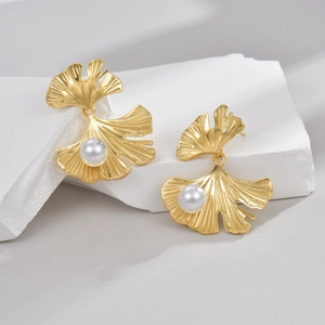 Golden ginkgo leaf earrings with pearls on a minimalist white stone background
