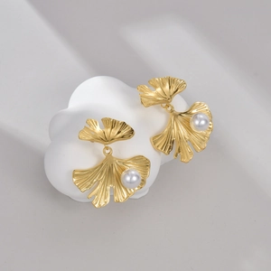 Detailed close-up of gold ginkgo leaf earrings with pearls on a cloud ceramic tray