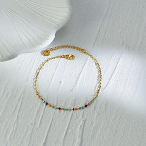 Gold stainless steel bracelet with colorful beads on a marble stone background