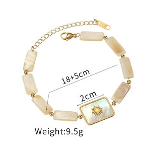 Bracelet perlé en acier doré avec breloques en nacre et pendentif soleil sur fond blanc