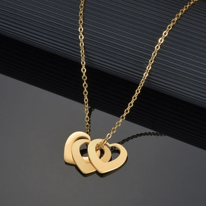 Collier en acier doré avec trois pendentifs en forme de cœur sur un fond noir texturé
