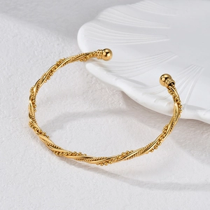 Detail of gold rope twist bangle with beads on white porcelain plate edge